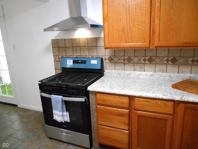 kitchen with wall chimney range hood, brown cabinetry, tasteful backsplash, and gas range