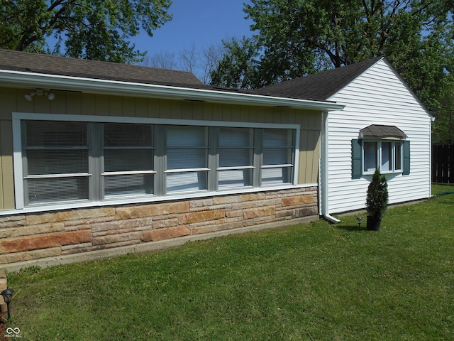 view of property exterior featuring roof with shingles, a yard, and stone siding