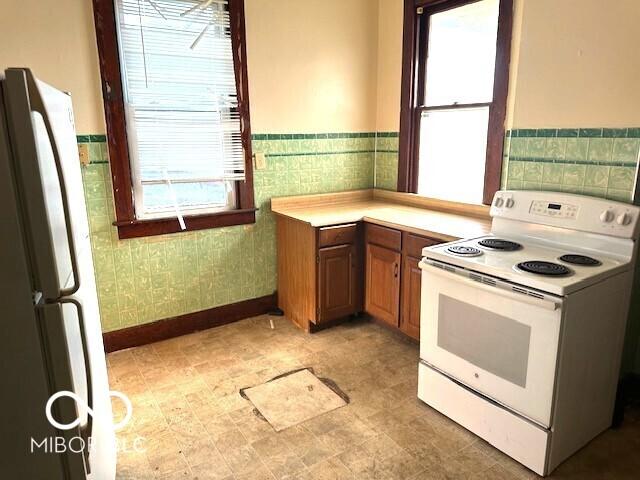 kitchen featuring light countertops, wainscoting, brown cabinets, and white appliances