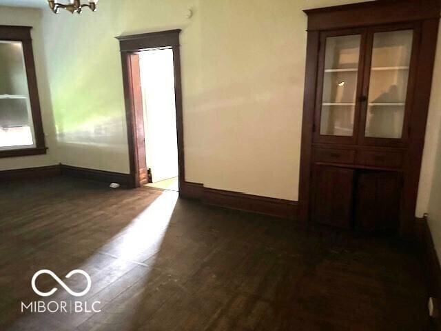 unfurnished room featuring baseboards, dark wood-style flooring, and a chandelier