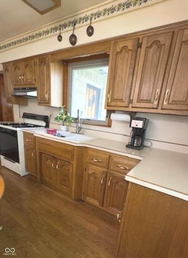 kitchen featuring under cabinet range hood, brown cabinets, white range with gas stovetop, and light countertops