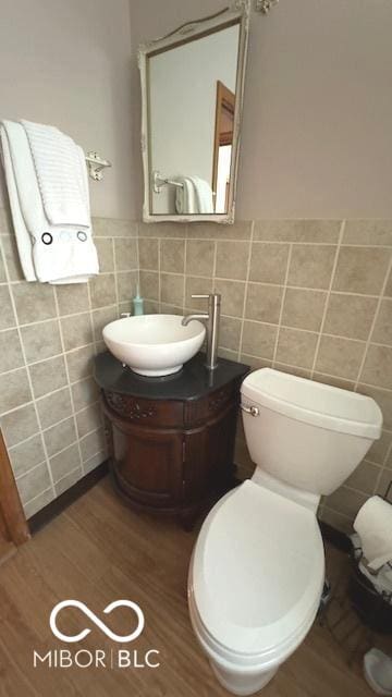 half bath with toilet, tile walls, wood finished floors, and vanity