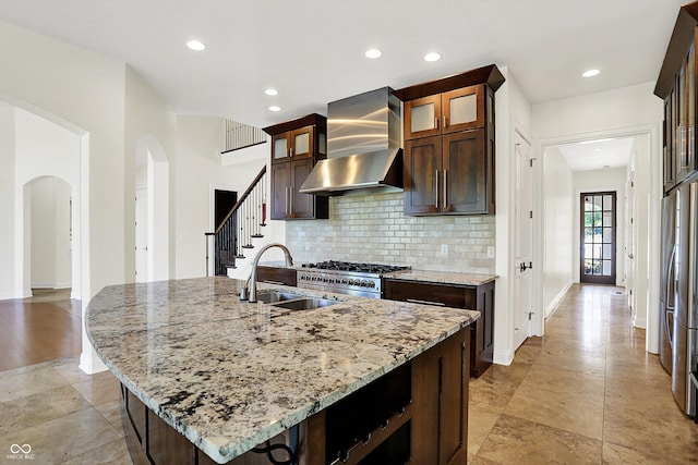 kitchen with wall chimney exhaust hood, arched walkways, a sink, backsplash, and stainless steel appliances