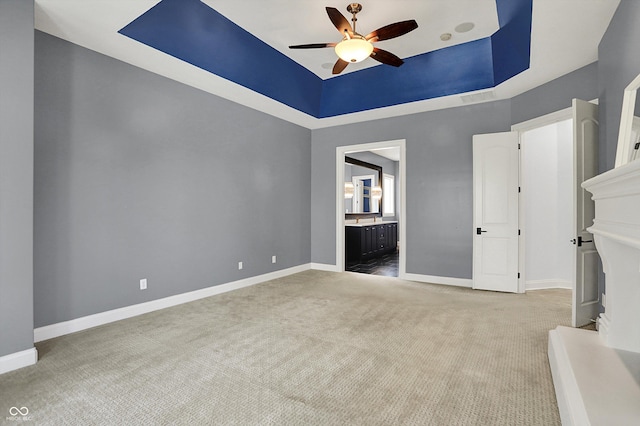 interior space featuring baseboards, ensuite bathroom, ceiling fan, a raised ceiling, and carpet flooring