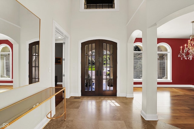foyer entrance with baseboards, a chandelier, french doors, and a towering ceiling