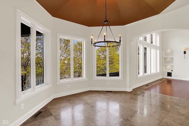 unfurnished dining area featuring visible vents, arched walkways, built in shelves, baseboards, and a chandelier
