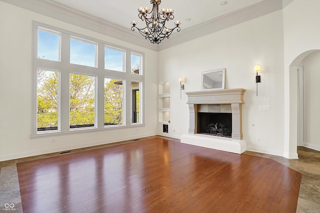 unfurnished living room featuring arched walkways, built in shelves, baseboards, a towering ceiling, and ornamental molding