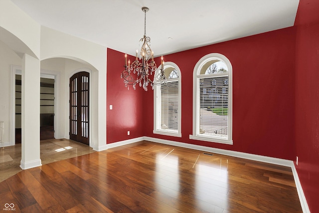 unfurnished dining area with arched walkways, baseboards, a chandelier, and wood finished floors