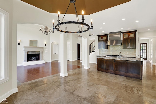 kitchen featuring wall chimney range hood, arched walkways, an inviting chandelier, and dark brown cabinets
