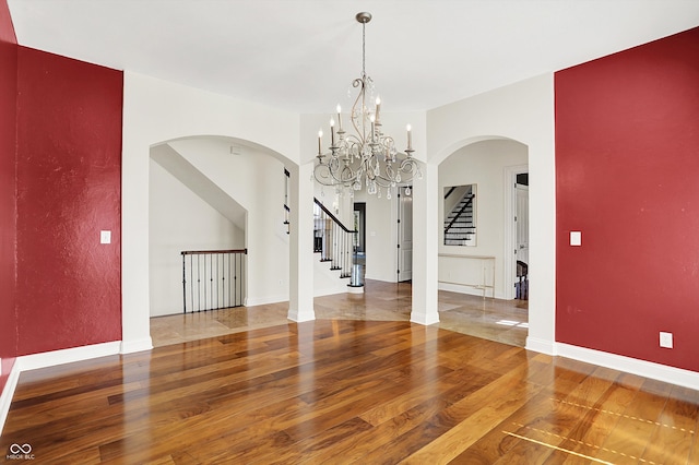 unfurnished dining area featuring an inviting chandelier, arched walkways, baseboards, wood finished floors, and stairway