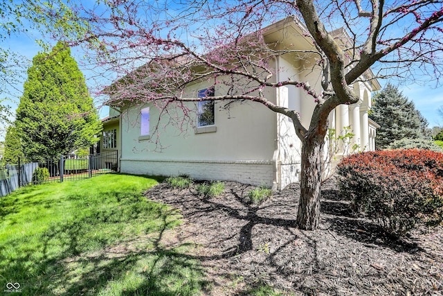 view of side of home with a yard, brick siding, fence, and stucco siding