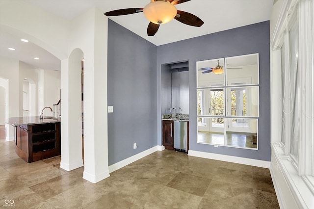 empty room featuring baseboards, arched walkways, a sink, and ceiling fan