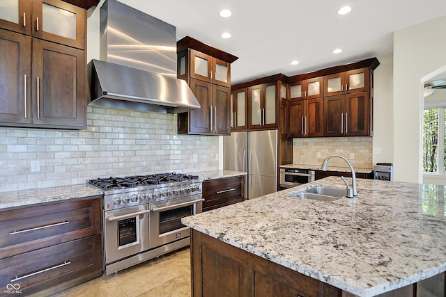 kitchen featuring light stone countertops, recessed lighting, wall chimney exhaust hood, a sink, and appliances with stainless steel finishes