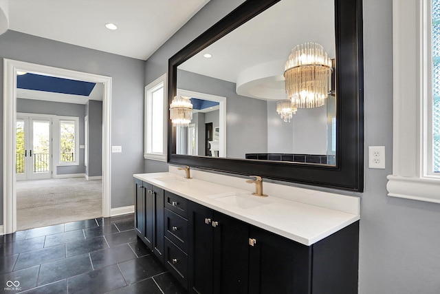 full bathroom with a sink, baseboards, an inviting chandelier, and double vanity
