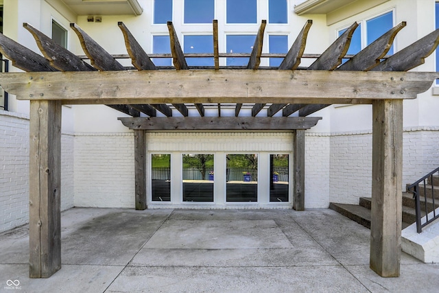 view of exterior entry featuring brick siding, a patio, and a pergola