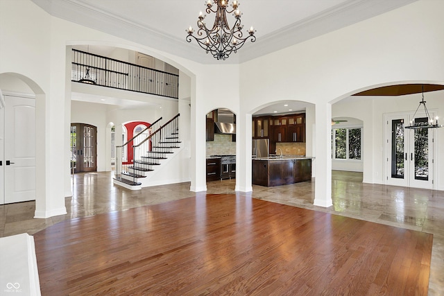 unfurnished living room featuring french doors, baseboards, an inviting chandelier, and wood finished floors