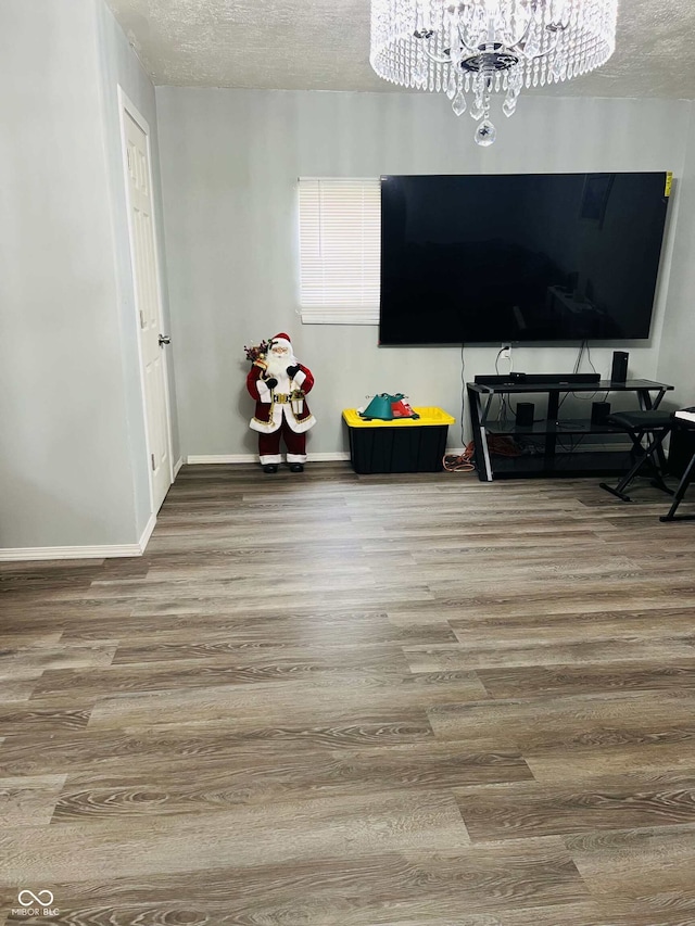interior space with baseboards, a textured ceiling, a notable chandelier, and wood finished floors