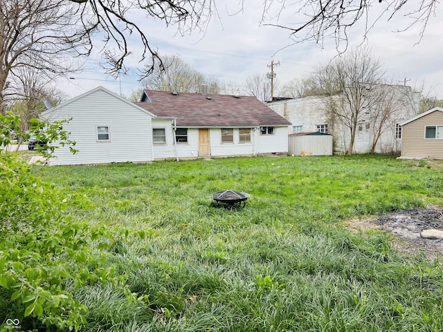 back of house featuring roof with shingles, an outdoor fire pit, a shed, a lawn, and an outdoor structure