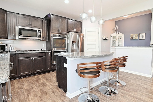 kitchen with dark brown cabinetry, light stone countertops, a breakfast bar, light wood-type flooring, and stainless steel appliances