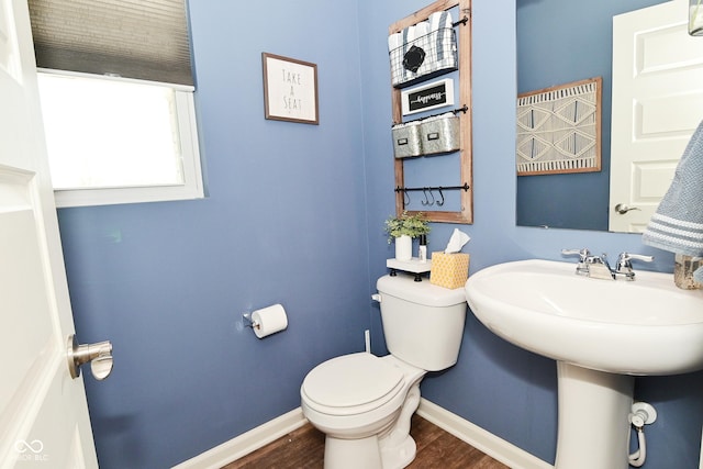 half bath with baseboards, wood finished floors, and toilet