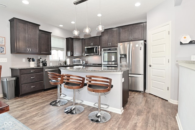 kitchen with dark brown cabinets, a breakfast bar area, stainless steel appliances, light wood-type flooring, and a kitchen island
