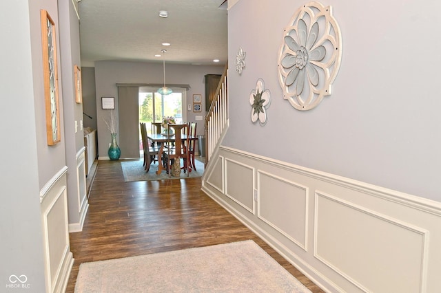 hall with stairs, a decorative wall, wood finished floors, and a wainscoted wall