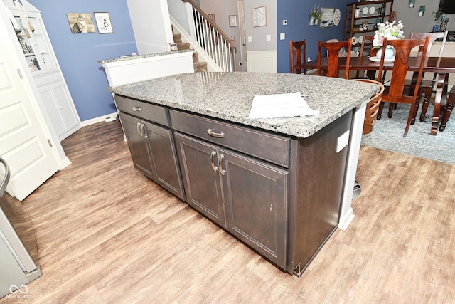 kitchen with light wood-type flooring, light stone counters, a kitchen island, and dark brown cabinets