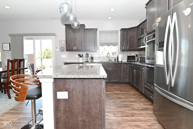 kitchen with a kitchen breakfast bar, appliances with stainless steel finishes, a center island, light stone countertops, and dark wood-style floors