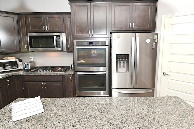 kitchen featuring tasteful backsplash, light stone countertops, stainless steel appliances, and dark brown cabinets