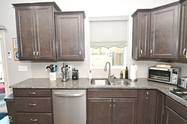 kitchen with dark brown cabinetry, tasteful backsplash, dishwasher, a sink, and dark stone countertops