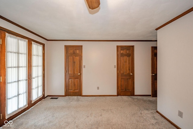 carpeted spare room featuring baseboards, ornamental molding, ceiling fan, and visible vents