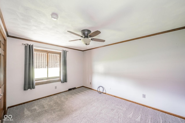 empty room with carpet flooring, a ceiling fan, baseboards, visible vents, and ornamental molding