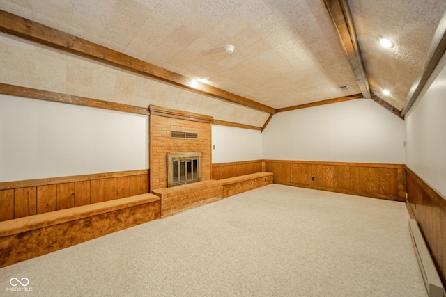 additional living space featuring wainscoting, baseboard heating, carpet floors, a brick fireplace, and vaulted ceiling with beams