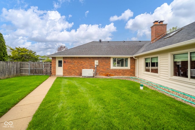 rear view of house with fence, a chimney, brick siding, a shingled roof, and a lawn