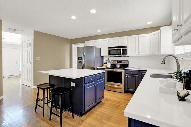 10746 Gateway Dr, Fishers, IN 46037 - kitchen featuring appliances with stainless steel finishes, blue cabinetry, a sink, a breakfast bar, and light wood-style flooring