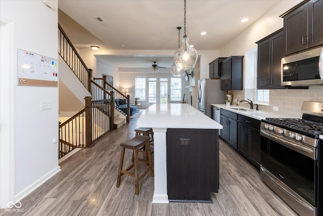 kitchen featuring wood finished floors, ceiling fan, a kitchen breakfast bar, a sink, and stainless steel appliances