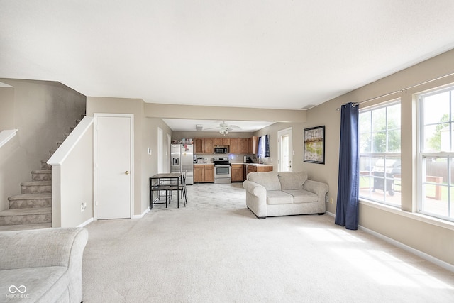 living area featuring stairway, baseboards, ceiling fan, and light carpet