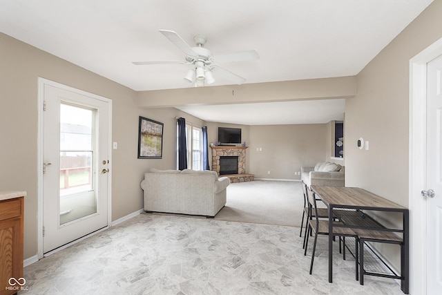 living room with baseboards, light colored carpet, a stone fireplace, and ceiling fan