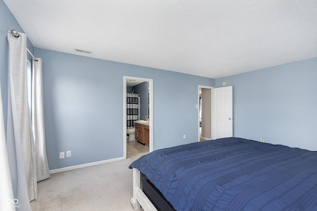 bedroom with baseboards, light colored carpet, ensuite bathroom, and visible vents