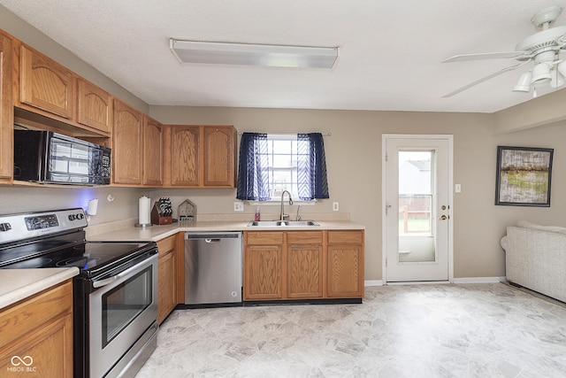 kitchen with brown cabinets, ceiling fan, a sink, light countertops, and stainless steel appliances