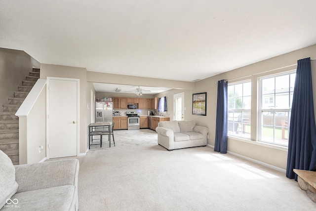 living area with baseboards, light carpet, a ceiling fan, and stairs