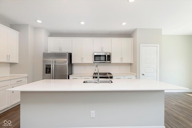 kitchen featuring dark wood-style flooring, appliances with stainless steel finishes, a sink, an island with sink, and tasteful backsplash