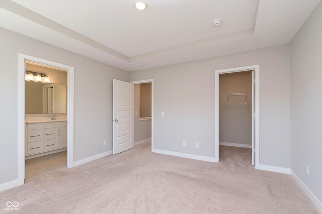 unfurnished bedroom featuring a walk in closet, baseboards, light carpet, and a raised ceiling