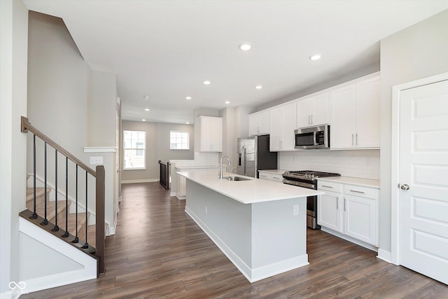kitchen with dark wood-style flooring, tasteful backsplash, a center island with sink, a sink, and stainless steel appliances