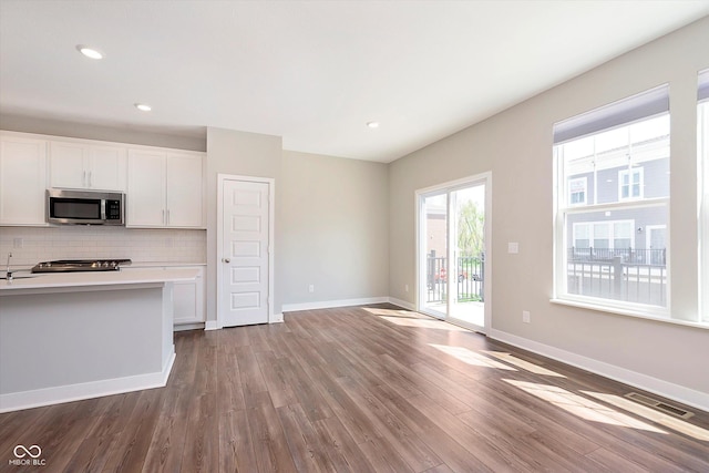 kitchen with white cabinets, light countertops, stainless steel microwave, wood finished floors, and visible vents