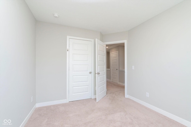 unfurnished bedroom featuring light colored carpet, baseboards, and a closet