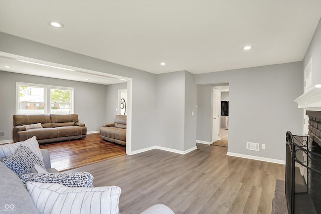 living room featuring baseboards, a fireplace, recessed lighting, and wood finished floors