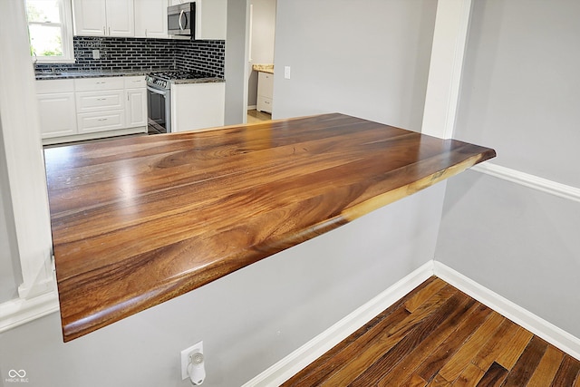 bar featuring backsplash, stainless steel appliances, baseboards, and dark wood finished floors