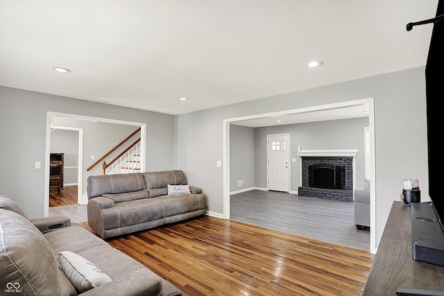 living area featuring a brick fireplace, wood finished floors, stairway, baseboards, and recessed lighting