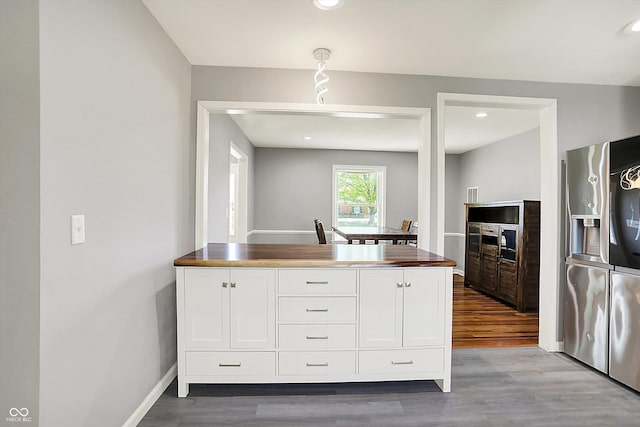 kitchen featuring stainless steel refrigerator with ice dispenser, baseboards, wood finished floors, and white cabinets